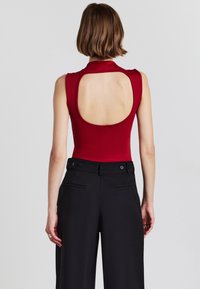 Body rosso senza maniche con design sulla schiena scoperta, abbinato a pantaloni neri a vita alta con una texture liscia e dettagli con bottoni.
