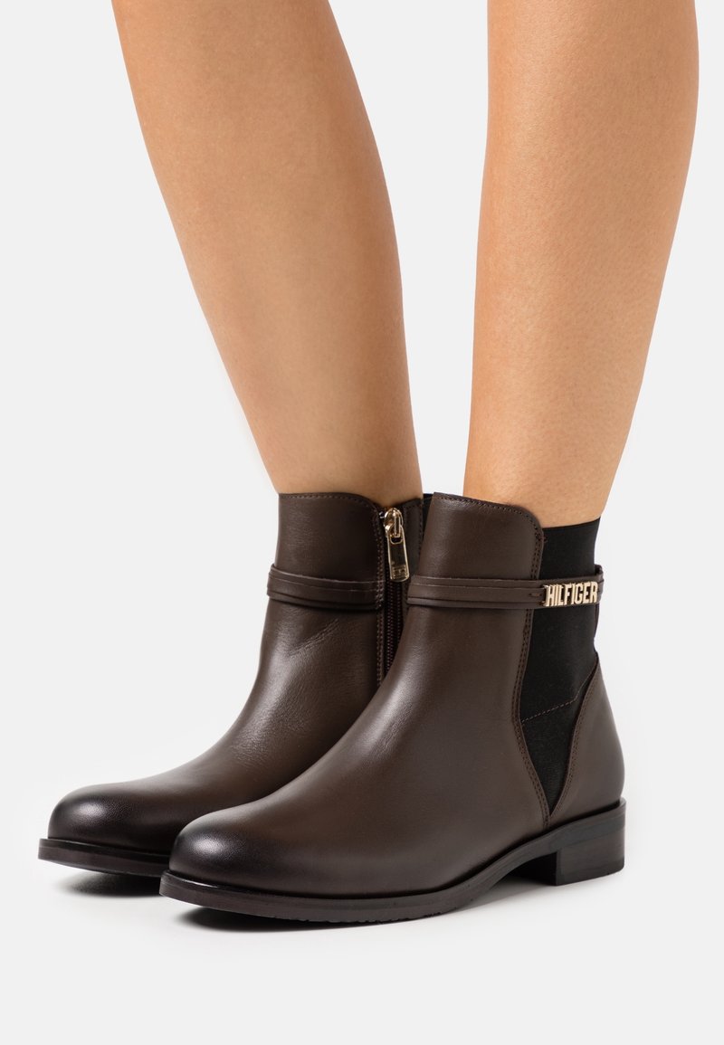 Bottines en cuir marron avec un panneau latéral élastique noir et des détails en métal doré. Présentent un bout arrondi et un petit talon carré.