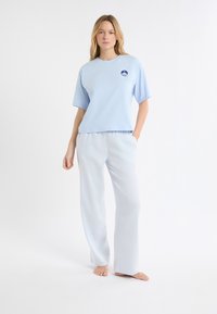 Jasnoniebieska bluzka z krótkim rękawem i okrągłym dekoltem z naszywką z logo, zestawiona z jasnoniebieskimi, szerokimi spodniami w kratę. Gładka faktura materiału.