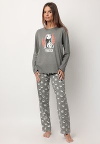 Sudadera de manga larga gris con un estampado gráfico y llamas naranjas, combinada con pantalones grises que presentan un patrón de calaveras en blanco y negro.