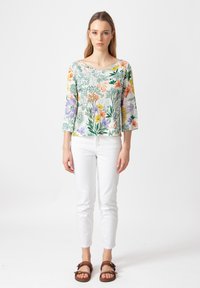 Lichtgewicht top met bloemenpatroon, een brede halslijn en driekwartmouwen, gecombineerd met witte slim-fit jeans en bruine sandalen.