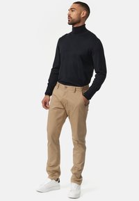 Chinos beige combinados con un suéter de cuello alto negro. Los chinos tienen un corte clásico con bolsillos laterales. El calzado son zapatillas blancas con detalles en negro.