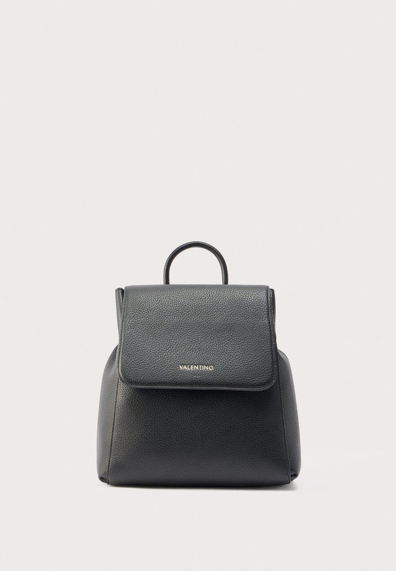 Mochila de cuero negro con un acabado texturizado, un asa superior y una solapa con cierre que presenta letras doradas. Forma compacta con bordes redondeados.