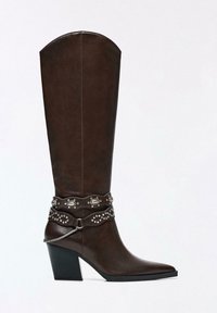 Ciemnobrązowy skórzany kozaki do kolan z zaostrzonym noskiem, masywnym obcasem i ozdobnymi metalowymi ćwiekami oraz łańcuchami wokół kostki.