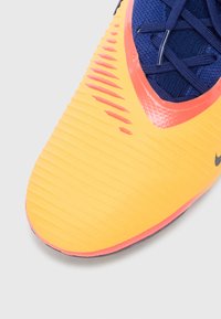 Nike athletic shoe featuring a yellow and orange textured upper, dark blue fabric accents, and a streamlined design with visible ridges.