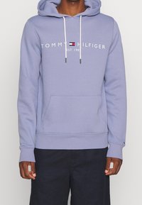 Felpa leggera viola chiaro in misto cotone, con tasca frontale a kangaroo, stringhe bianche e logo "TOMMY HILFIGER" sulla parte anteriore.