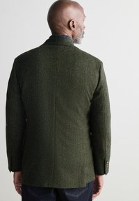 Grüner Fischgrät-Tweed-Blazer mit Reverskragen und knöpfbaren Manschetten, ausgestattet mit einer strukturierten Oberfläche und einem taillierten Schnitt.