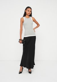 Top cinzento sem mangas com acabamento branco, combinado com uma saia maxi preta e saltos pretos pontiagudos. Pequena mala preta com alça na mão.