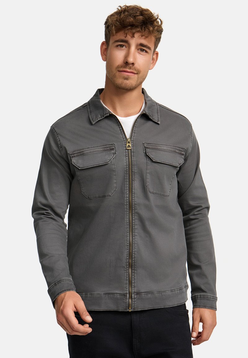 Grå zip-up jakke med to brystlommer, spids krave og stikninger. Stoffet virker glat og har en let slidt tekstur.
