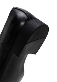 Zwarte leren enkelboot met een ronde neus, gestructureerde bovenkant en een vlakke rubberen zool. Zichtbare stiksels en slanke ontwerpdetaillering verbeteren het profiel.