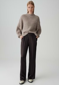 Maglione lavorato a maglia beige con collo alto e vestibilità ampia, abbinato a pantaloni marrone scuro, fluidi. Presenta un design a vita alta e una leggera lucentezza.