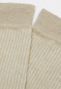 Beige Rippensocken mit glitzernder Textur, die ein gewebtes Design und einen umgeschlagenen Bund für zusätzliche Details aufweisen.