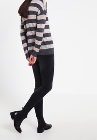Maglione a righe grigio e beige con maniche lunghe, abbinato a jeans skinny neri e stivaletti, visto da dietro.