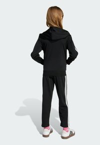 Svart zip-up hoodie med huva, ihop med matchande svarta byxor med vita sidostreck. Vita sportskor med rosa strumpor.