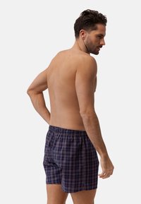 Marineblaues Karomuster bei den Badeshorts mit elastischem Bund, lockerer Passform und Seitentaschen. Das Muster umfasst hellblaue und lila Quadrate.