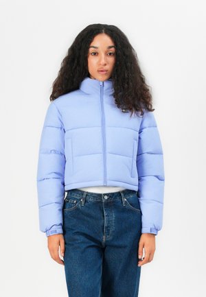 Lichtpaarse cropped pufferjack met een hoge kraag, horizontaal gequilt ontwerp en ritssluiting aan de voorkant; gecombineerd met donkerblauwe jeans.
