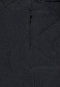Tela negra acolchada con un patrón de diamantes, que presenta una cremallera oculta. La textura parece ligeramente arrugada y suave.