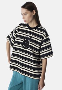 Camiseta de rayas de gran tamaño en negro y crema con mangas cortas, que presenta un diseño gráfico texturizado en negro en el centro.