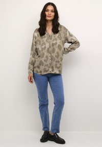 Blusa beige de corte suelto con un sutil estampado de leopardo, escote en V, mangas largas, combinada con jeans rectos de color azul claro y mocasines negros.