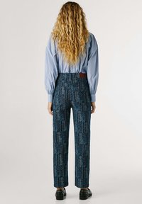 Blue patterned trousers with a high waist and straight legs, featuring intricate floral designs and a fabric tag at the back.