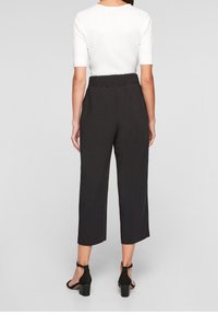 Pantalons noirs coupés avec une taille élastique, texture lisse et coupe large, associés à un top blanc à manches courtes et des escarpins noirs.