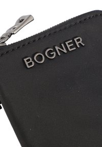 Czarny portfel z tkaniny o chropowatej powierzchni, z wyraźnym logo "BOGNER" oraz metalowym suwakiem do zamykania.