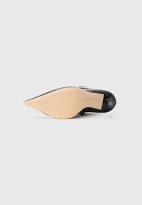 Black patent leather high-heeled shoe with a pointed toe and a beige sole, featuring a bow accent near the heel. Smooth texture.