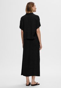 Ensemble en lin noir comprenant une chemise courte à manches courtes ample et une jupe longue avec fente latérale, tous deux avec une finition mate texturée.