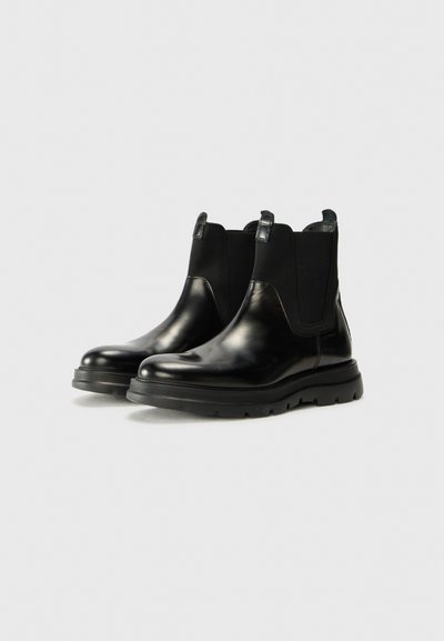 Bottines Chelsea en cuir noir avec panneaux élastiques sur les côtés, bout rond et semelle en caoutchouc texturée. Présente des languettes pour un enfilage facile.