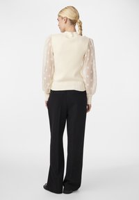 Pull crème avec des manches bouffantes à pois, texture côtelée et silhouette ajustée, associé à un pantalon large noir.