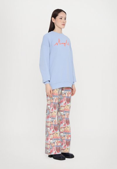Light blue oversized sweatshirt with red cursive text, paired with wide-legged pants featuring a collage print in pink, blue, and red. Black shoes.