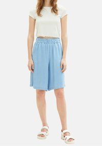 Lichtblauwe, knielange shorts met een elastische tailleband en zijzakken. Gepaard met een witte cropped top en witte platform sandalen.