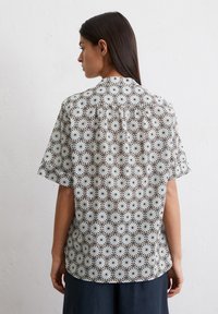 Chemise à manches courtes à motif floral avec des dessins circulaires en blanc, marron et bleu, dotée d'un col standard et d'une coupe décontractée.