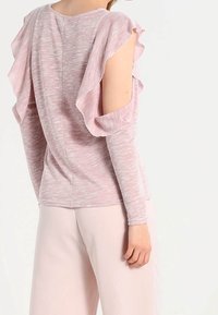 Haut rose clair avec des manches à volants et des manches longues ajustées. Tissu doux et texturé avec un col rond, et une couture arrière lisse.