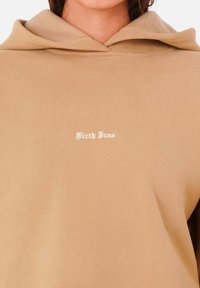 Sudadera con capucha marrón, de textura suave y diseño relajado. Presenta el texto blanco "Sixth June" en el frente.