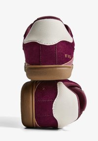 Baskets en daim et cuir avec un dessus bordeaux profond et un talon en cuir blanc. Forme arrondie, surface texturée et semelle en caoutchouc marron.