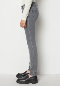 Harmaat farkut, jotka ovat kapeat ja puolivälin vyötäröllä, takaosassa taskut ja hienoinen haalistuminen. Yhdistettynä mustiin slip-on-kengiin.