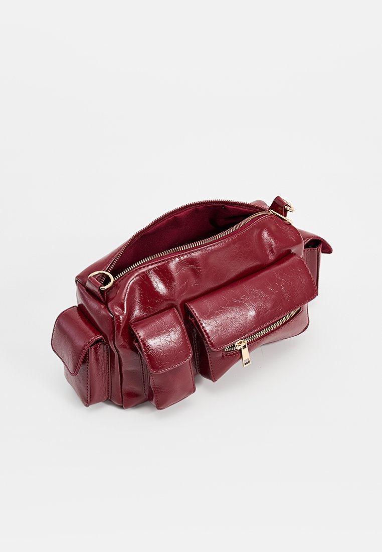 Burgunder-farbenes Kunstledertasche mit einem Reißverschluss, zwei Vordertaschen und goldfarbener Hardware; glatte Textur mit einem kompakten rechteckigen Design.