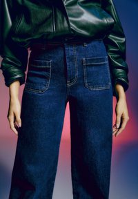 Jean en denim bleu foncé taille haute avec deux poches avant, un fil léger et une coupe décontractée, associé à une veste en cuir noire.