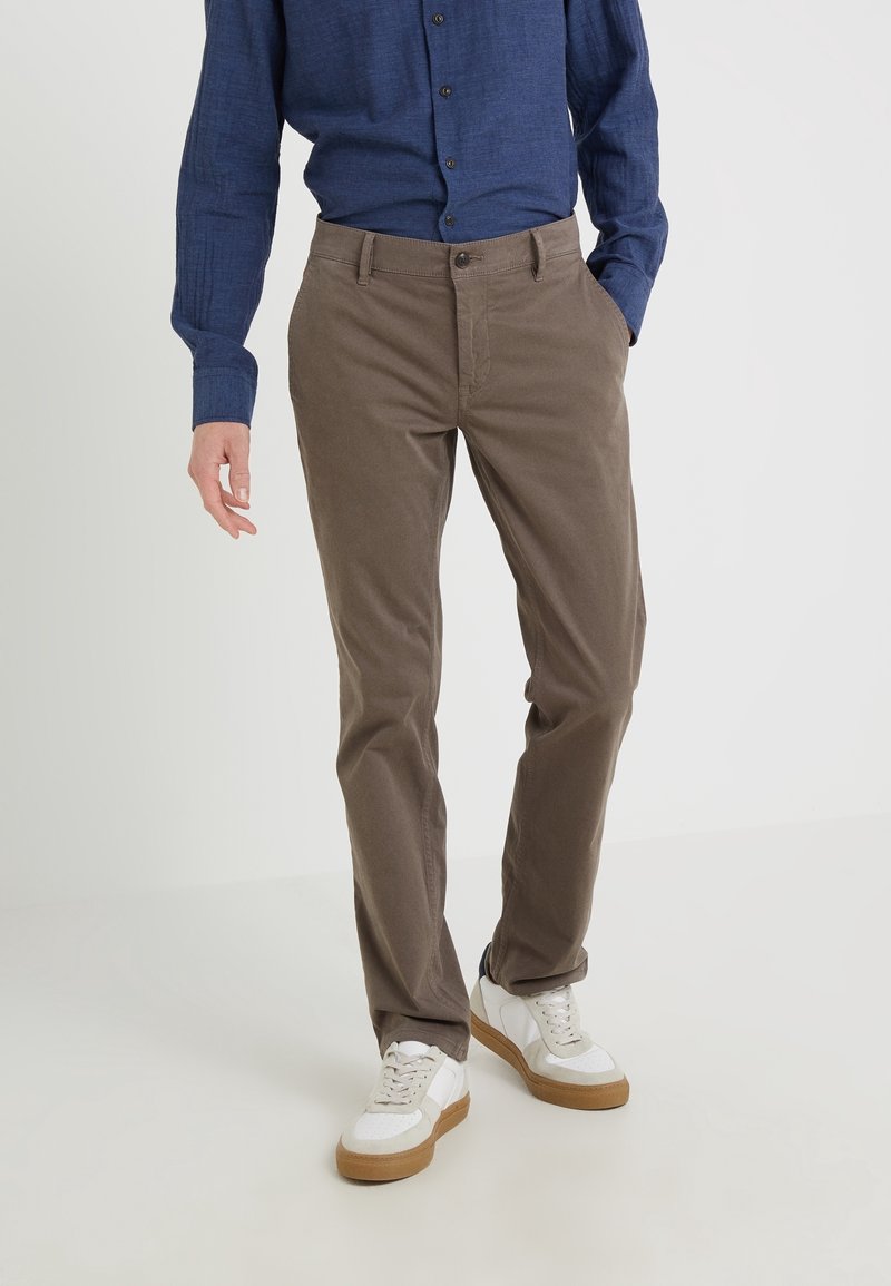 Bruna bomullschinos med rak skärning, med sid- och bakfickor, bärs tillsammans med en blå knapp-up skjorta och vita sneakers.