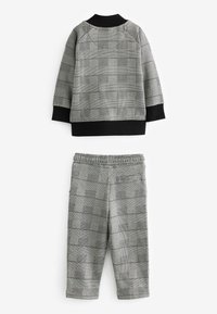 Grå rutig tvådelad outfit som består av en långärmad topp med svarta accenter och matchande byxor med elastisk midja.