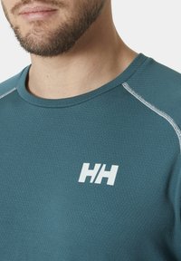 Mintel sportshirt met een gestructureerd patroon, voorzien van witte stiksels langs de schouders en een wit logo op de borst.