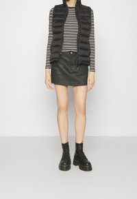 Gilet invernale nero, maglietta a maniche lunghe a righe, minigonna di jeans verde con orlo sfrangiato e stivali da combattimento neri con lacci.