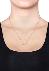 Rose gold halskæde med uendelighedssymbol og hjerte-design. Kæden er delikat og slank, og hviler på en bar hals mod en sort top.