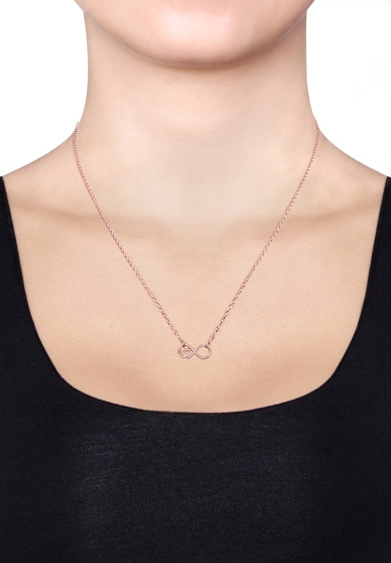 Rose gold halskæde med uendelighedssymbol og hjerte-design. Kæden er delikat og slank, og hviler på en bar hals mod en sort top.