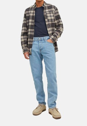 Plaid flannel shirt in beige and black over a navy t-shirt, paired with light blue jeans and beige suede shoes. Classic fit and casual style.