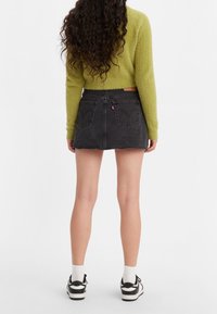 Svart denimkjol med fransad nederkant, ihop med en limegrön, strukturerad kortärmad tröja och svart-vita sneakers med ankelsockor.