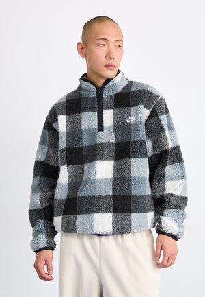 Fleece genser med svart, grå og hvit rutemønster; halv-zip krage; Nike-logo på venstre bryst; strukturert, mykt materiale; avslappet passform.