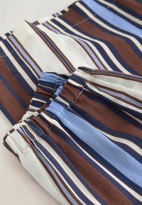 Tissu avec bords élastiqués présentant des rayures horizontales de couleur brun, bleu, blanc et bleu clair.