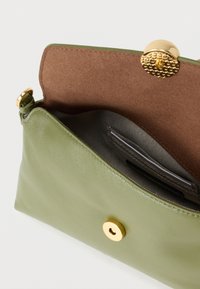 Zöld bőr kézitáska texturált arany gombzárral. Belsejében barna bélés és strukturált rekeszek találhatók a rendezettség érdekében.